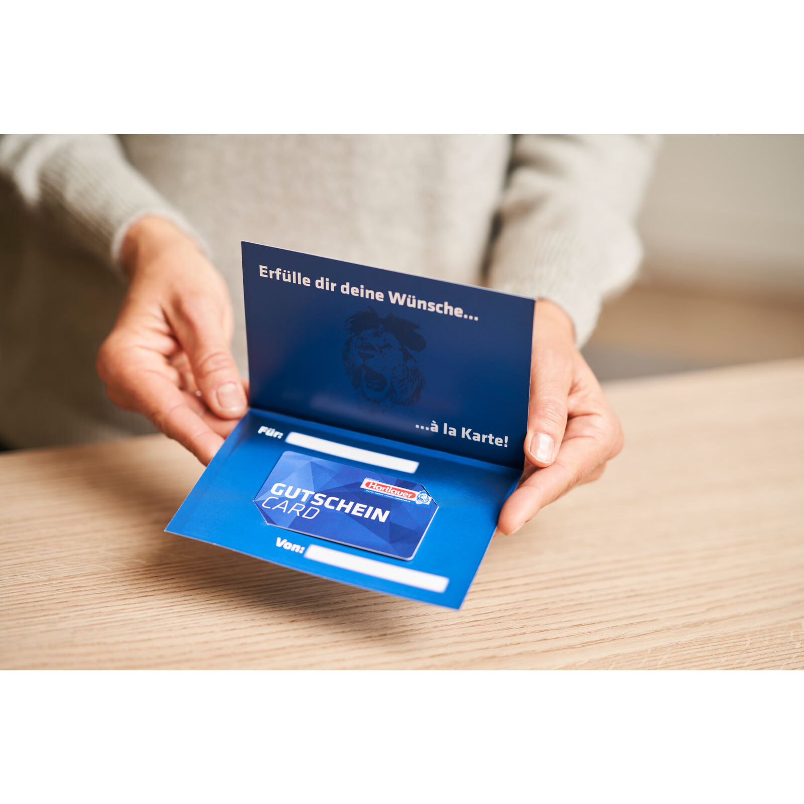 Hartlauer Gutscheincard im passenden Umschlag wird von zwei H&auml;nden gehalten