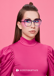 Junge Frau mit auffälligem Makeup und auffälliger Kioto Nakamura Brille, in pinkem Top vor pinkem Hintergrund.