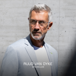 Ein elegant gekleideter Mann steht vor einer Mauer, blickt in die Ferne und trägt eine Brille der Marke Ruud van Dyke.Auf der Grafik steht folgender Text: "Ruud van Dyke Bruxelles"