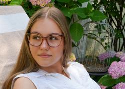Eine junge Frau posiert an einem sonnigen Tag in einem Garten, während sie Brillen von Mila ZB trägt.