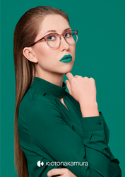 Junge Frau mit auffälligem Makeup und auffälliger Kioto Nakamura Brille, in grünem Top vor grünem Hintergrund.