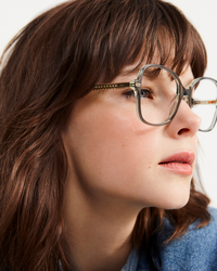 Junge Frau mit blauem Top und Lancel Acetat schmetterlings Brille vor weißem Hintergrund.