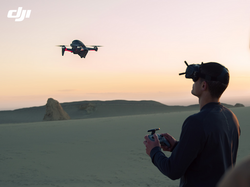 "Mann mit VR-Brille und Fernbedienung steuert vor Zuseherin eine DJI Drohne in Landschaft bei Dämmerung"