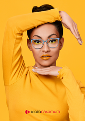 Junge Frau mit auffälligem Makeup und auffälliger Kioto Nakamura Brille, in gelbem Top vor gelbem Hintergrund.