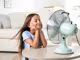 Mädchen sitzt vor Tischventilator im Wohnzimmer