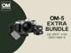 Ein OM-5 Extra Bundle bestehend aus der Kamera, einem Objektiv, einem Akku und einem Griff befindet sich auf einem olivgrün beigen Hintergrund. Daneben steht folgender Text: "OM-5 Extra Bundle im Wert von über € 600,-."