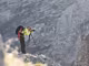 Ein Mann steht auf einem Felsen in einem Gebirge und fotografiert mit einer Kamera.
