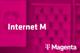 Tarif Internet M und Magenta-Logo vor unscharfem magentafarbenem Hintergrund mit Handyabteilung in Hartlauer Geschäft