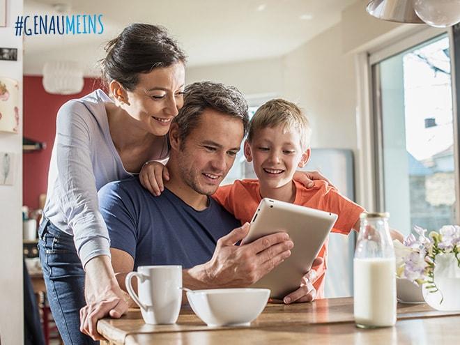 Vater, Mutter und Sohn surfen lächelnd im Internet auf einem Tablet am Küchentisch