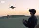 Mann mit VR-Brille und Fernbedienung steuert eine DJI Drohne in Landschaft bei Dämmerung