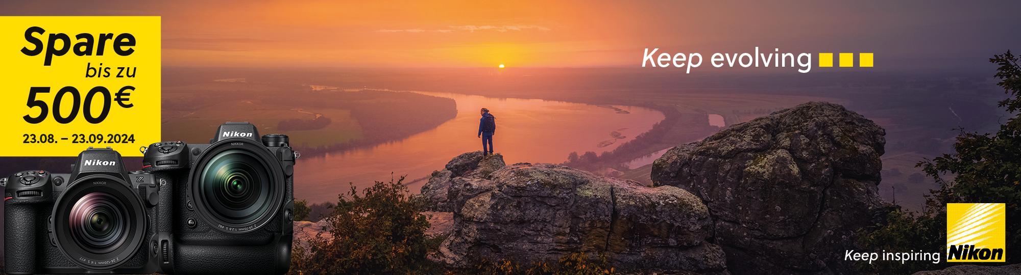 Grafik zur Bewerbung der Nikon Sofortrabatt Aktion. Im Hintergrund ist eine Person auf einem Berggipfel mit Sicht auf einen Fluss bei Sonnenaufgang zu sehen. Im Vordergrund sind die Produktbilder von zwei Nikon Kameras abgebildet. Auf der Grafik steht folgender Text: "Spare bis zu 500€. 23.08.-23.09.2024. Keep evolving. Keep inspiring. Nikon."