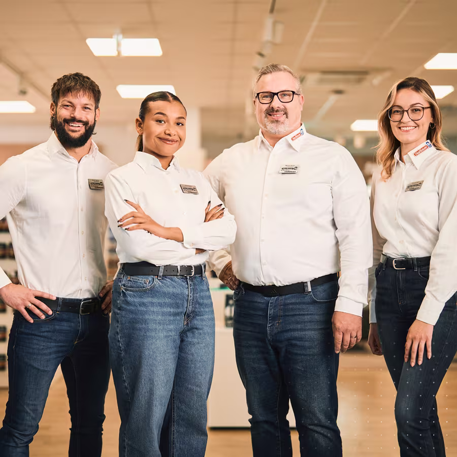 "Zwei Mitarbeiter und zwei Mitarbeiterinnen stehen in einem Hartlauer Geschäft und lächeln."