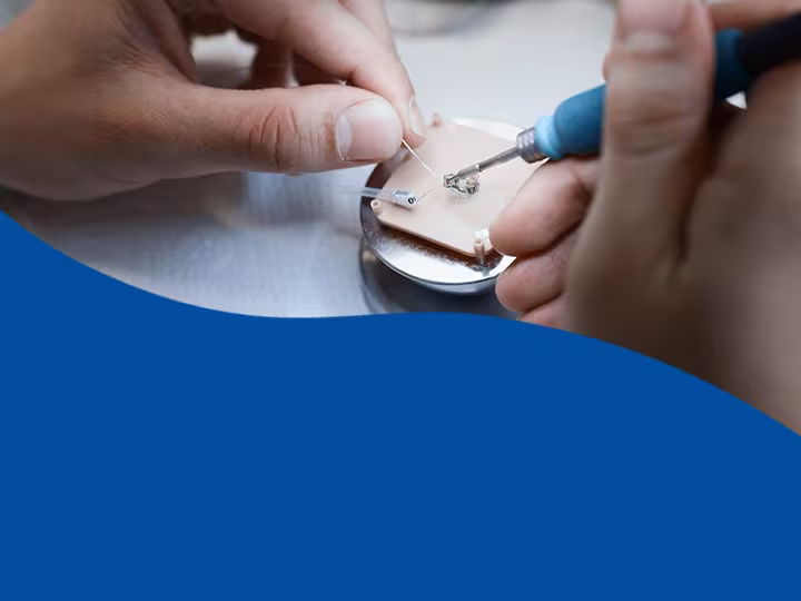 "Nahaufnahme eines Prozesses bei der Herstellung eines Hörgerätes. Auf der Grafik befindet sich folgender Text: \"Einfach Mehr. Hörgeräte Bauarten & Bauformen.\""