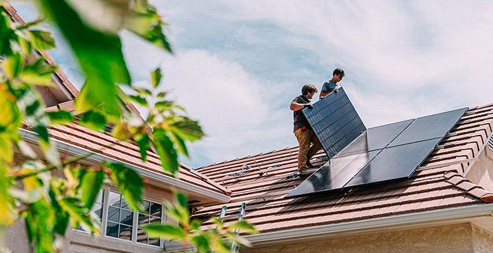 Zwei Männer befestigen Solarpanele auf einem Hausdach