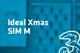 Tarif Drei Ideal Xmas SIM M und Drei-Logo vor unscharfem türkisem Hintergrund mit Handyabteilung in Hartlauer Geschäft