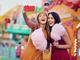  zwei lächelnde Frauen mit Zuckerwatte in der Hand machen ein Selfie vor einem Fahrgeschäft 