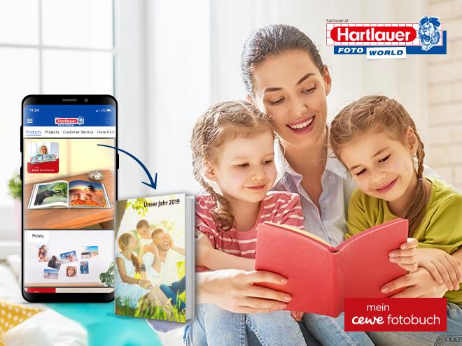 eine Mutter und zwei Kinder blättern in einem Buch, am Smartphone ist die Hartlauer Foto World abgebildet 