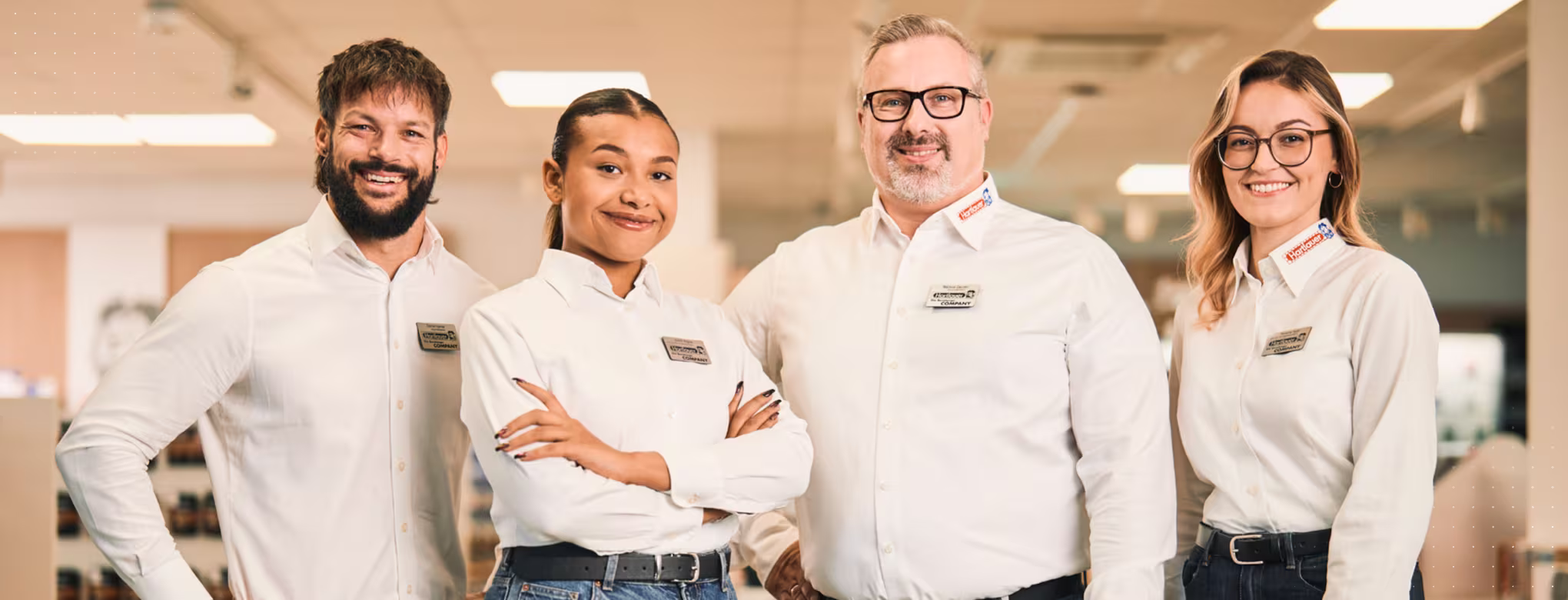 "Zwei Mitarbeiter und zwei Mitarbeiterinnen stehen in einem Hartlauer Geschäft und lächeln."