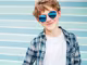 lächelnder Junge mit gespiegelter Sonnenbrille von Hartlauer vor gestreiftem Hintergrund