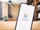 schwarzes Smartphone mit Google Lens Logo am Bildschirm vor Holzfläche und verschwommenem Interieur