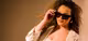 Junge Frau mit Locken, in weißem Blazer gekleidet , modelt mit Calvin Klein Sonnenbrille 
