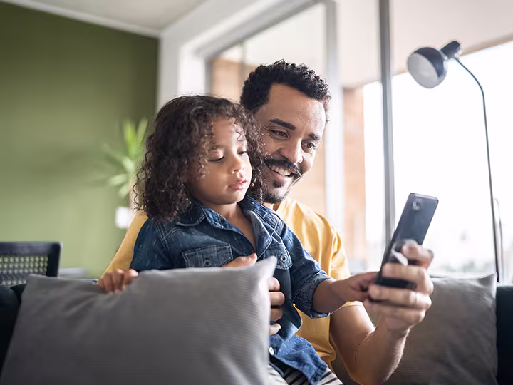 Vater und Tochter auf der Couch mit einem schwarzen Smartphone in der Hand 