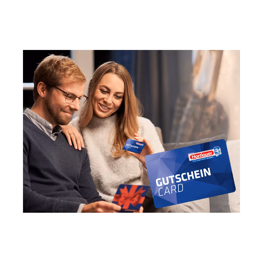 Glückliches Pärchen sitzt auf einem Sofa und hält die Hartlauer Gutscheincard in den Händen.