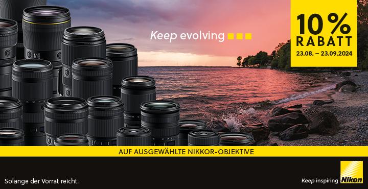 Grafik zur Bewerbung der Nikon -10% Objektivwochen. Auf der Grafik sind viele nebeneinander gereihte Objektive zu sehen. Der Hintergrund zeigt einen Kieselstrand bei Sonnenuntergang mit einigen Bäumen. Auf der Grafik steht folgender Text: "Keep evolving. 10% Rabatt 23.08. bis 23.09.2024. Auf ausgewählte Nikkor-Objektive. Solange der Vorrat reicht. Keep inspiring. Nikon."