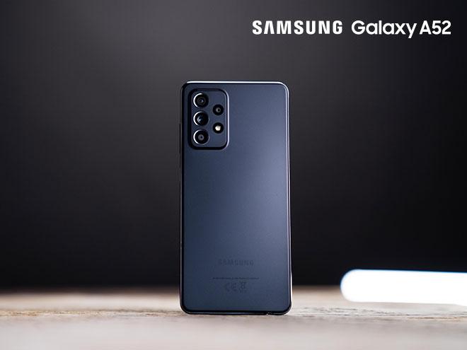 Rückseite eines SAMSUNG Galaxy A52 in Schwarz hochkant auf hölzerner Tischplatte stehend