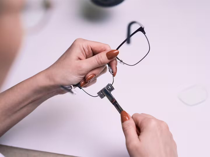 Auf der Grafik sind Frauenhände zu sehen, welche eine Brille halten. Bei der Brille werden die Gläser getauscht.