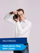 Ein Hartlauer Mitarbeiter hält eine Kamera neben seinen Kopf. Darunter steht folgender Text: "Multimedia. Mach deinen Weg beim Löwen."