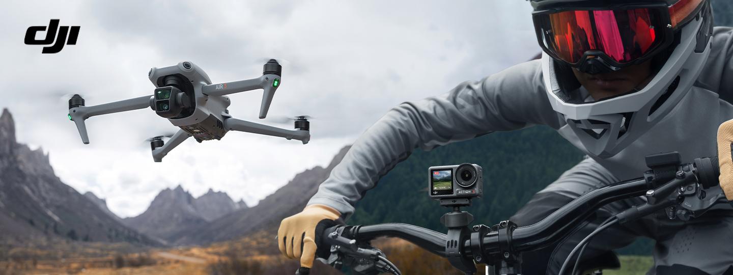  DJI Air 3 Kameradrohne beim Flug über hügeligem Gelände mit trockenem Gras und Downhill-Fahrer mit montierter Osmo Action 4 Action-Kamera