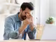 Mann vor Laptop mit Hand vorm Gesicht und einer Brille in der anderen Hand