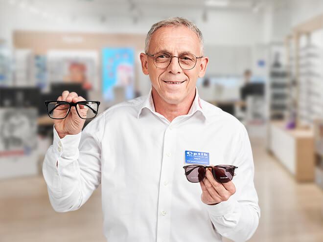 ein älterer Hartlauer Optiker hält eine Seh- und eine Sonnenbrille in den Händen
