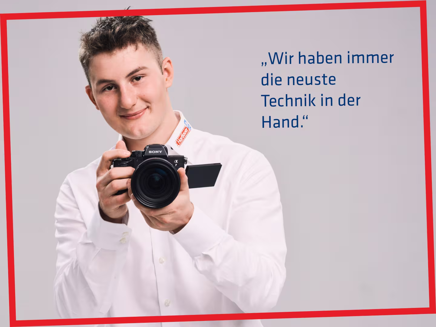 Ein Hartlauer Mitarbeiter hält eine Kamera in seinen Händen. Neben ihm befindet sich eine Sprechblase mit folgendem Text: "Wir haben immer die neueste Technik in der Hand." Die Grafik hat einen roten Rahmen.