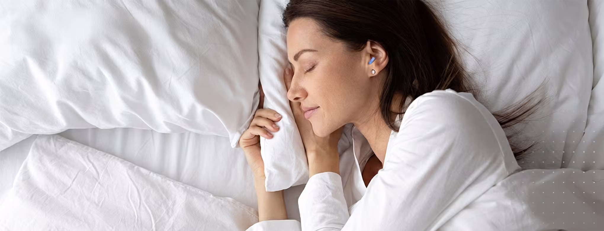 Frau liegt schlafend in einem Bett, sie tr&auml;gt Schlafschutz im Ohr; zufriedener Gesichtsausdruck