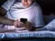 Ein Mann liegt im Bett und schaut auf sein Smartphone.